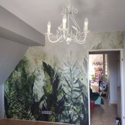 REMONTOWO Piotr Kania - Pokój z fototapetą z motywem dżungli, kremowy żyrandol z kryształkami, drewniana podłoga i widok na pokój dziecięcy w tle.