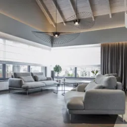 Jasny salon z szarymi sofami, drewnianą podłogą, oknami z roletami w kasecie i oryginalnymi lampami sufitowymi w kształcie wachlarzy.