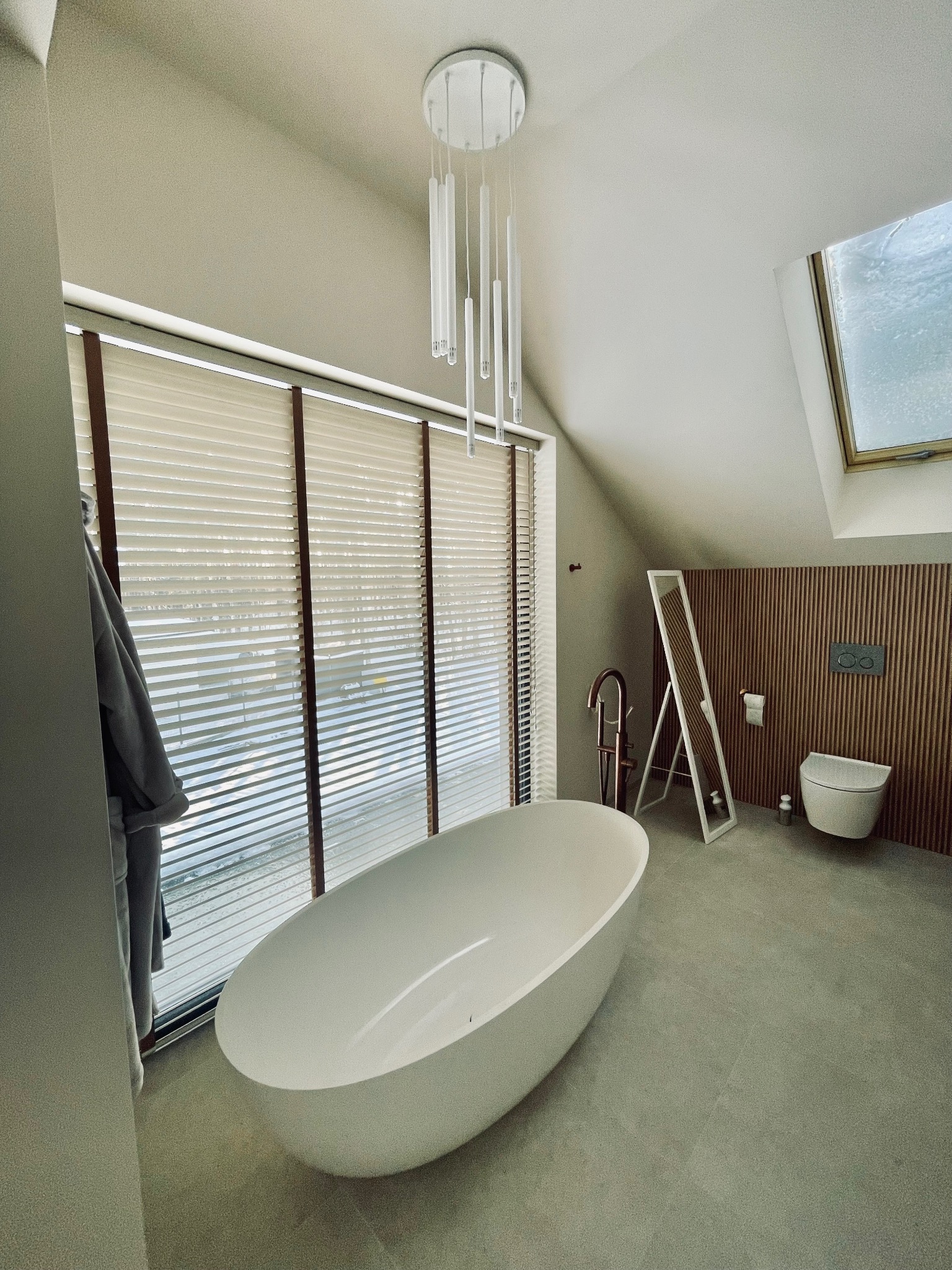 Nowoczesna łazienka na poddaszu z wolnostojącą wanną, drewnianymi żaluzjami w oknach i dekoracyjną ścianą z drewnianych paneli.