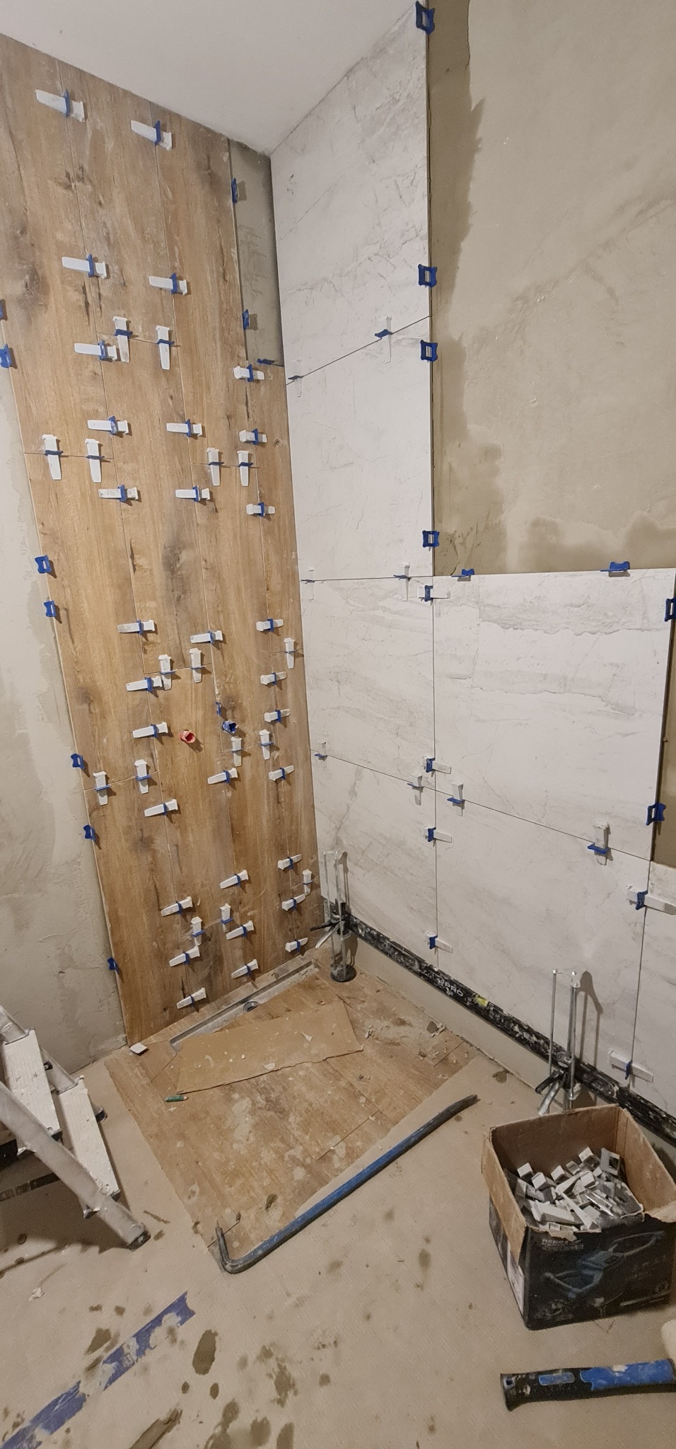 Montaż płytek imitujących drewno i białych płytek w trakcie prac wykończeniowych w łazience, widoczne narzędzia glazurnicze i system poziomowania płytek.