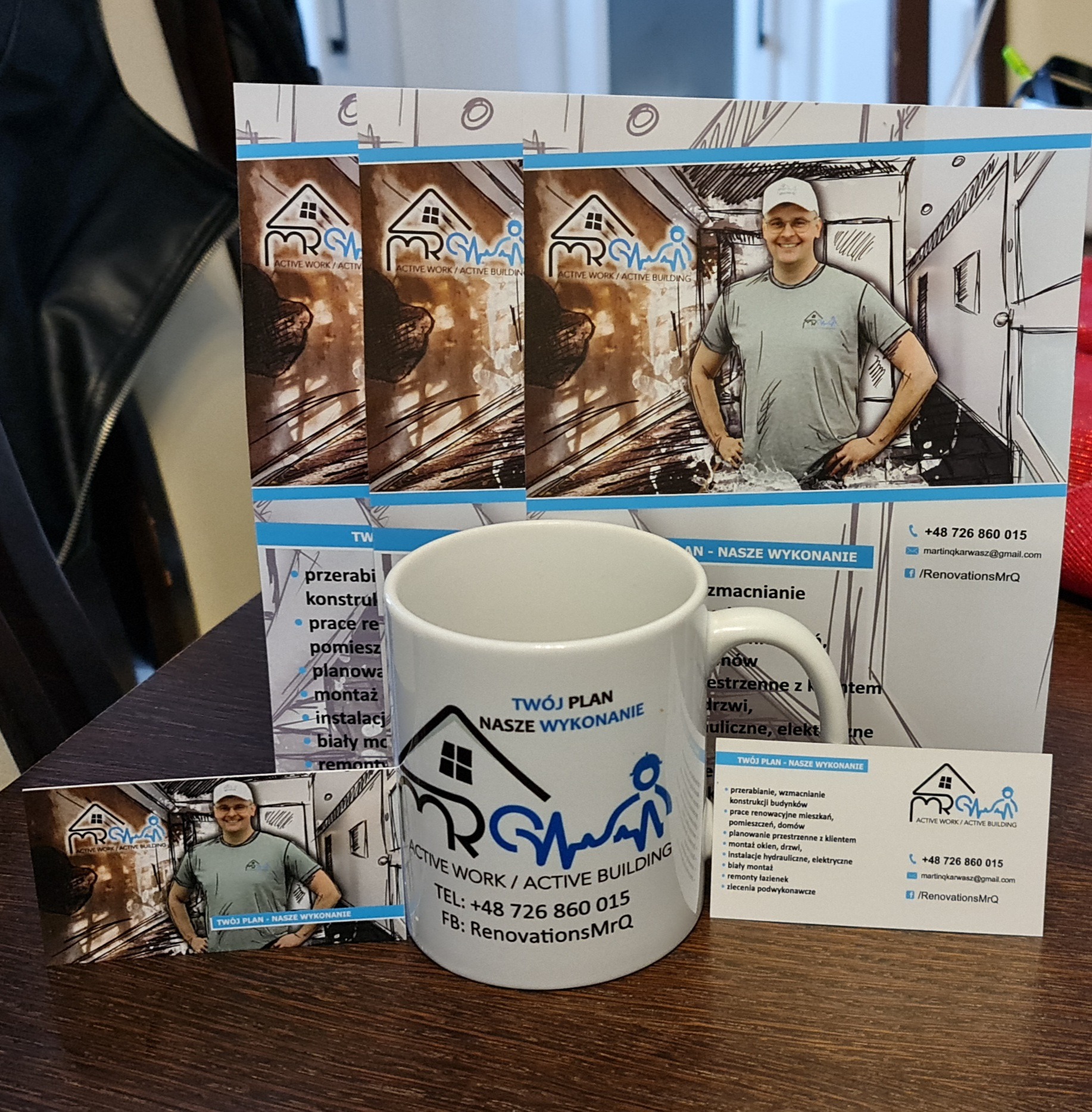 Materiały reklamowe firmy remontowej: wizytówki, ulotki i kubek z logo na drewnianym stole.