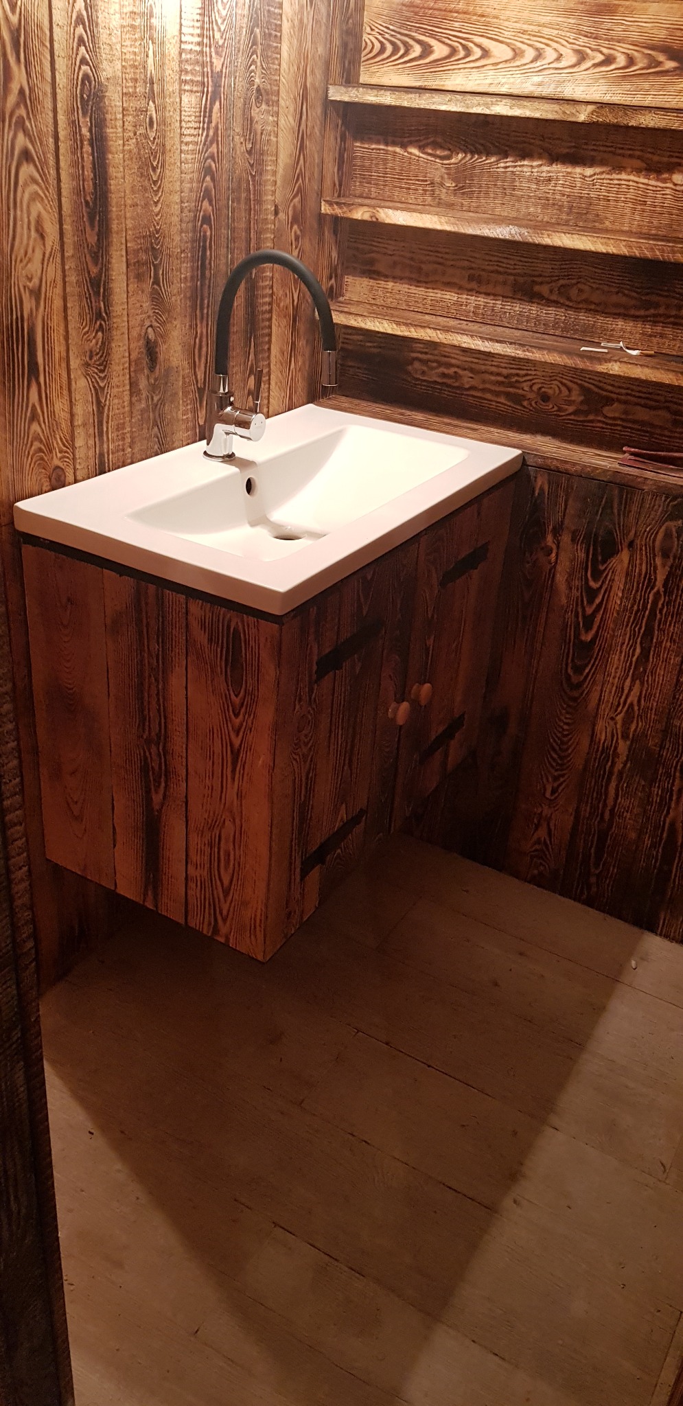 Biała umywalka z czarną baterią w łazience wykończonej drewnem z widocznymi półkami.