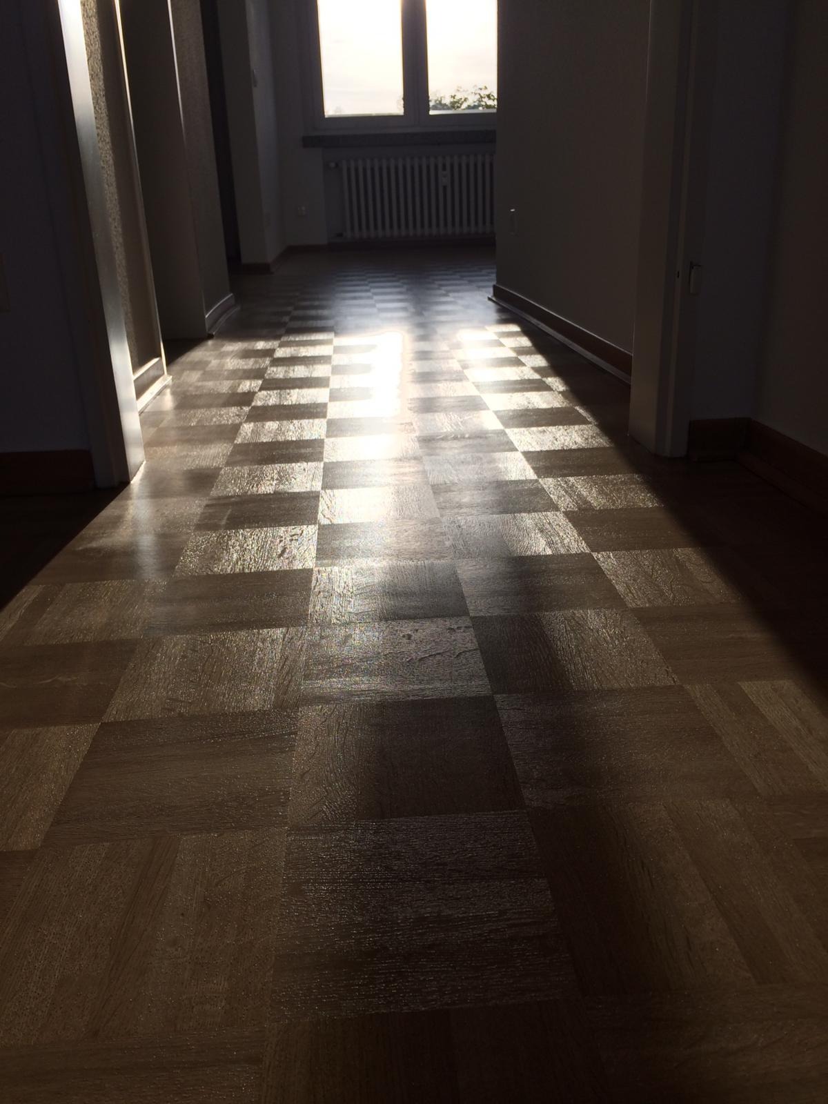 Szachownica z parkietu w pustym pokoju, oświetlona promieniami słońca padającymi przez okno.