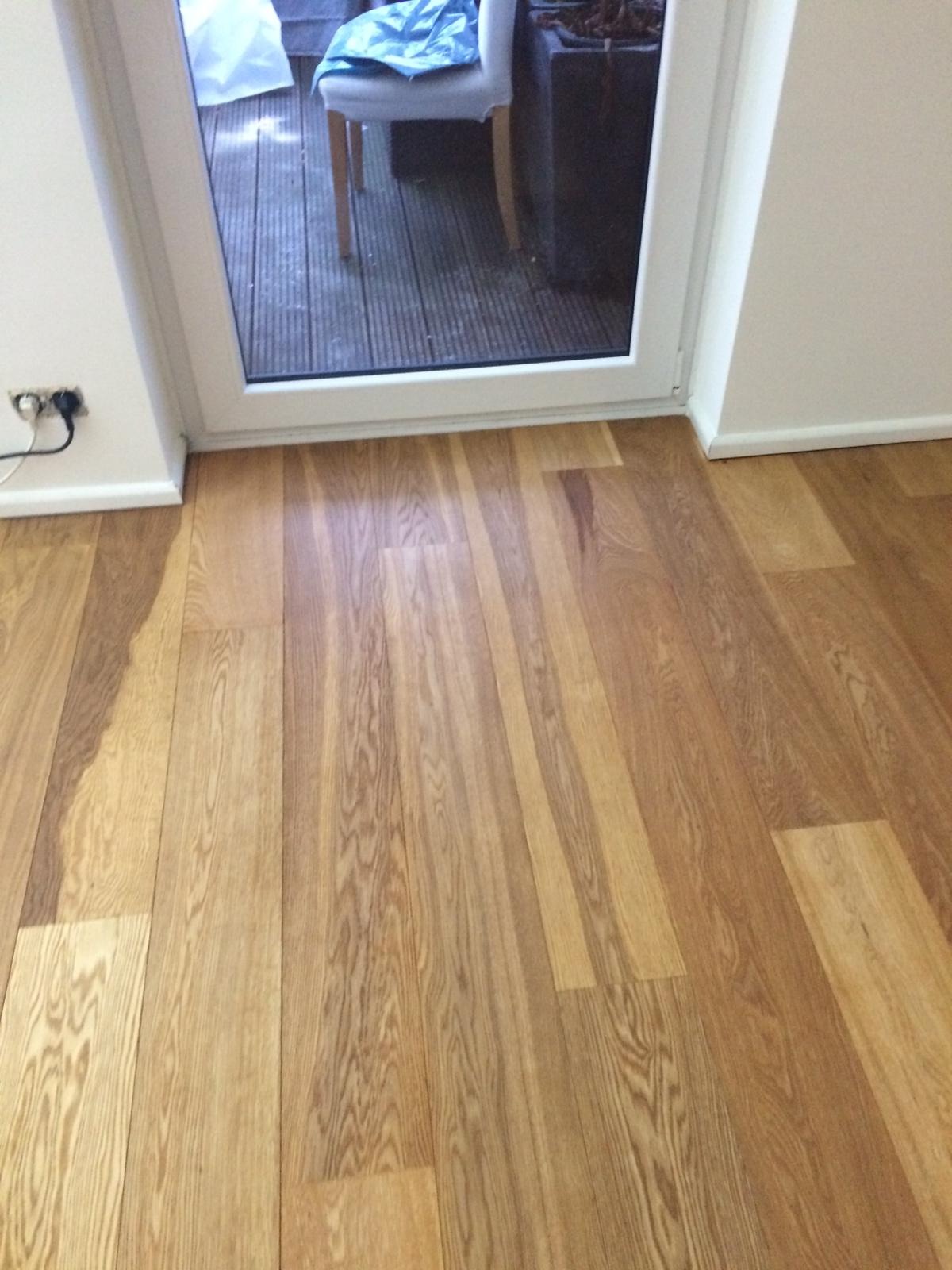 Jasna, drewniana podłoga ułożona wzdłuż białych drzwi balkonowych z widokiem na taras. Widoczny fragment gniazdka elektrycznego przy listwie przypodłogowej.