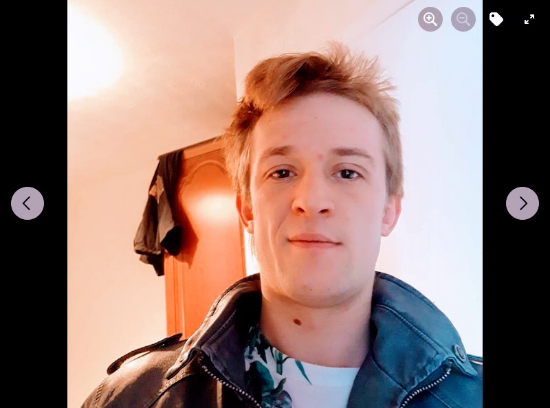 Portret młodego mężczyzny w skórzanej kurtce na tle pokoju z szafą.