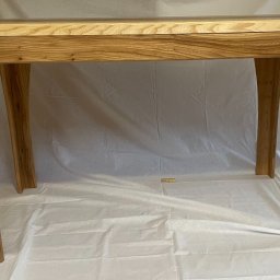 Adam Sułkowski - Surowy drewniany stół z wyraźnym usłojeniem, ustawiony na białym płótnie, eksponujący unikalny kształt nóg.