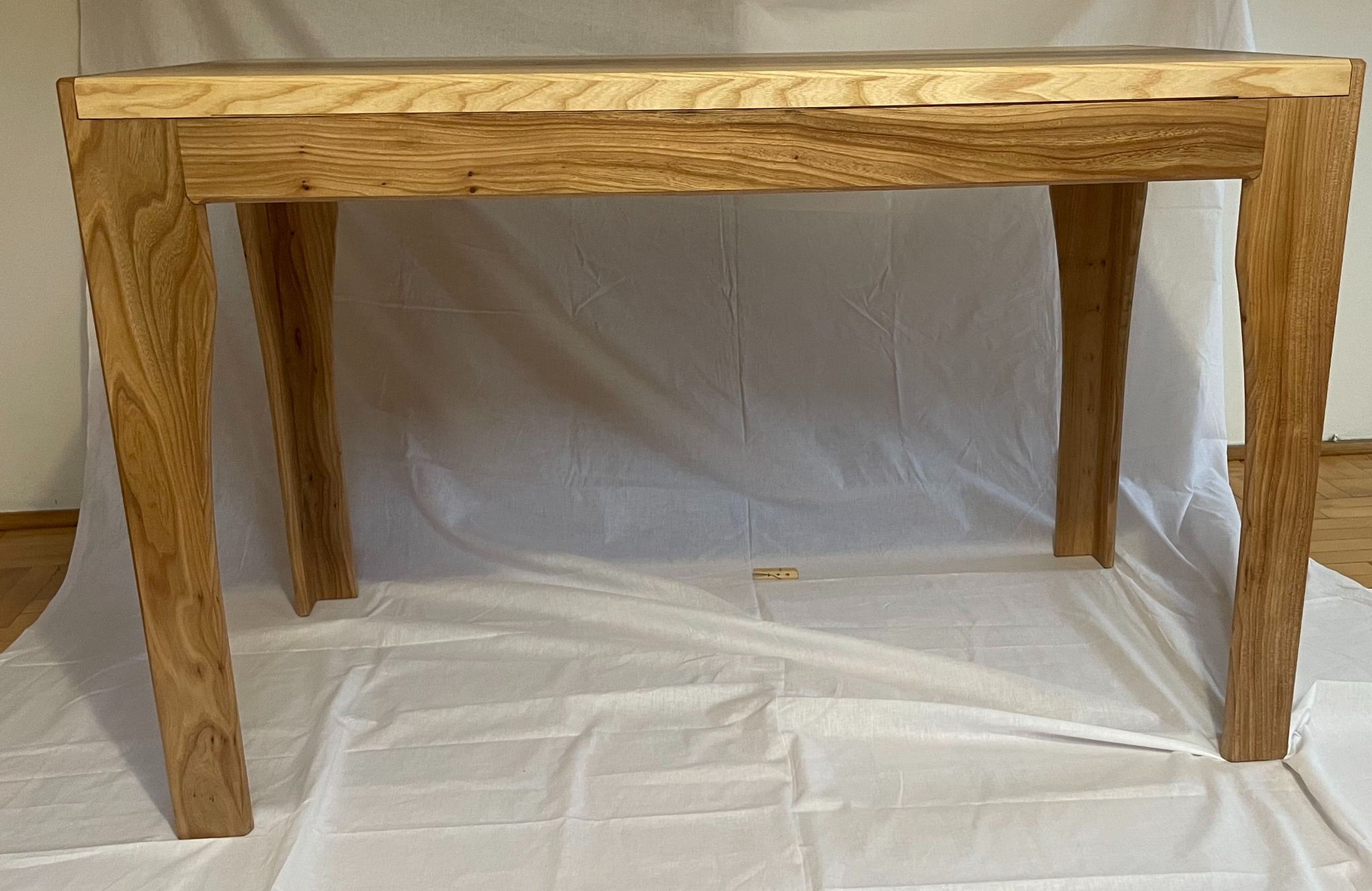 Surowy drewniany stół z wyraźnym usłojeniem, ustawiony na białym płótnie, eksponujący unikalny kształt nóg.