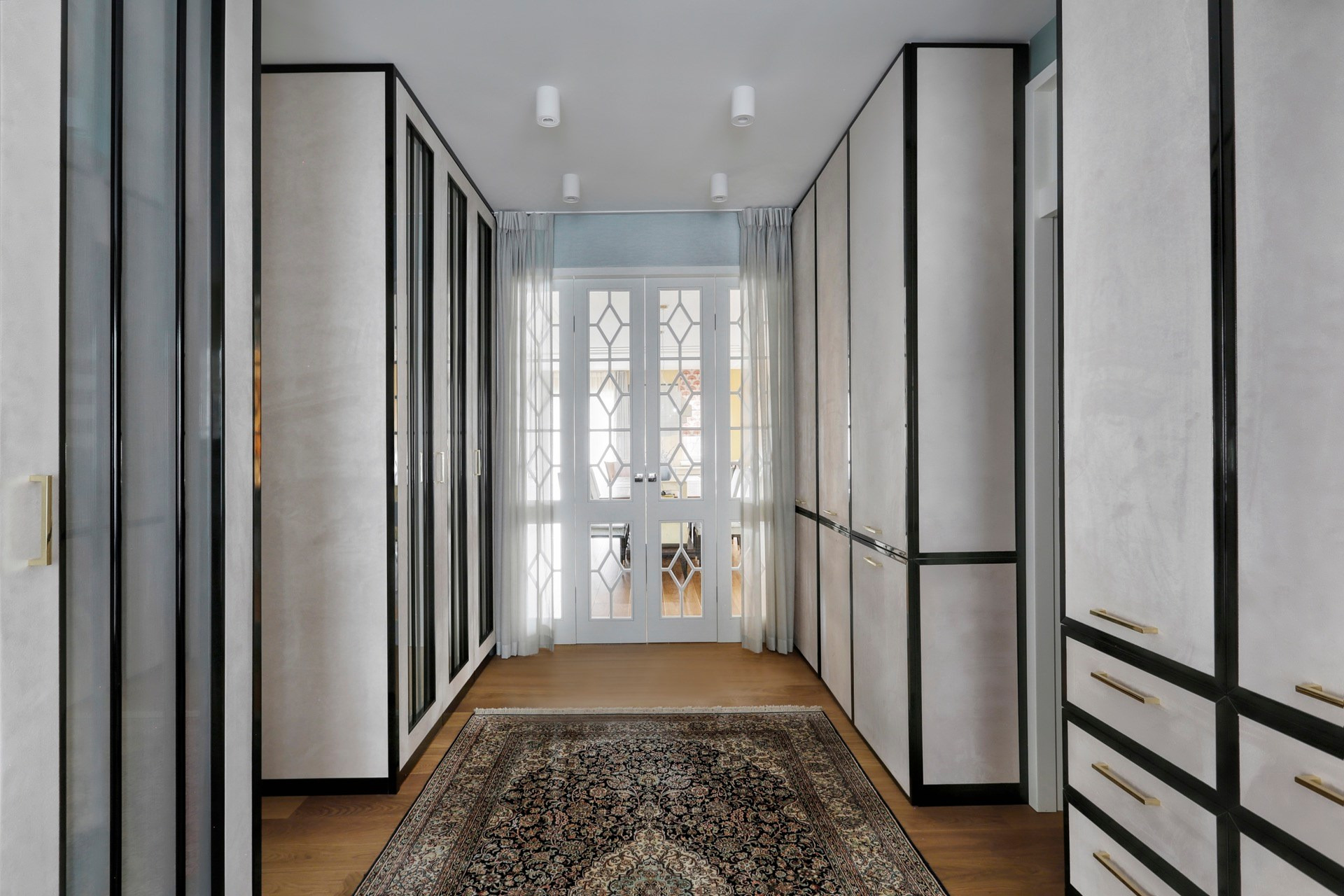 Korytarz z zabudową szaf wnękowych po obu stronach, dywan na podłodze i przeszklone drzwi na końcu.