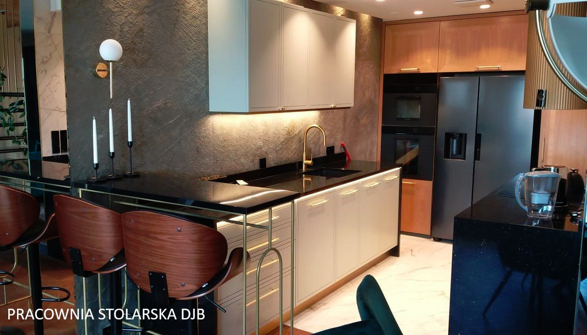 Nowoczesna kuchnia z białymi szafkami, czarnym blatem, złotą armaturą i oświetleniem LED, uzupełniona o drewniane krzesła barowe i dekoracyjne świece.