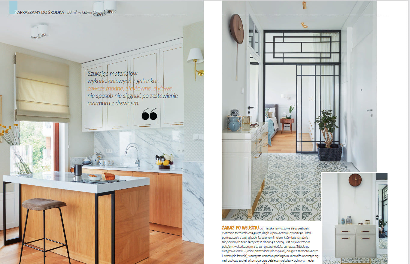 Nowoczesne wnętrze mieszkania: otwarta kuchnia z wyspą, marmurowy blat, drewniane szafki, przeszklone drzwi do sypialni, wzorzysta podłoga, komoda z mosiężnymi uchwytami.