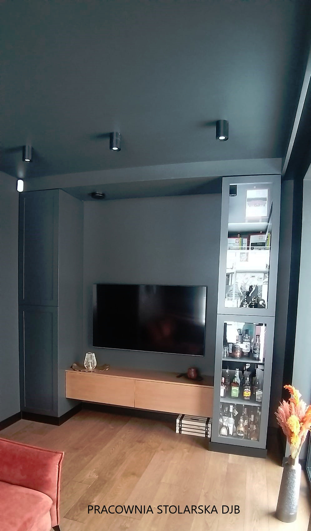 Nowoczesny salon z zabudową meblową w odcieniach szarości, obejmującą szafę, szafkę RTV z drewnianym frontem i przeszkloną witrynę barową z oświetleniem punktowym.