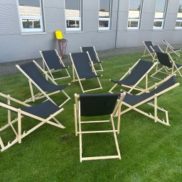 PERSEID SPÓŁKA Z OGRANICZONĄ ODPOWIEDZIALNOŚCIĄ - Rozstawione leżaki plażowe z czarnym materiałem na trawie przed budynkiem z oknami. Konfiguracja gotowa na wydarzenie plenerowe.