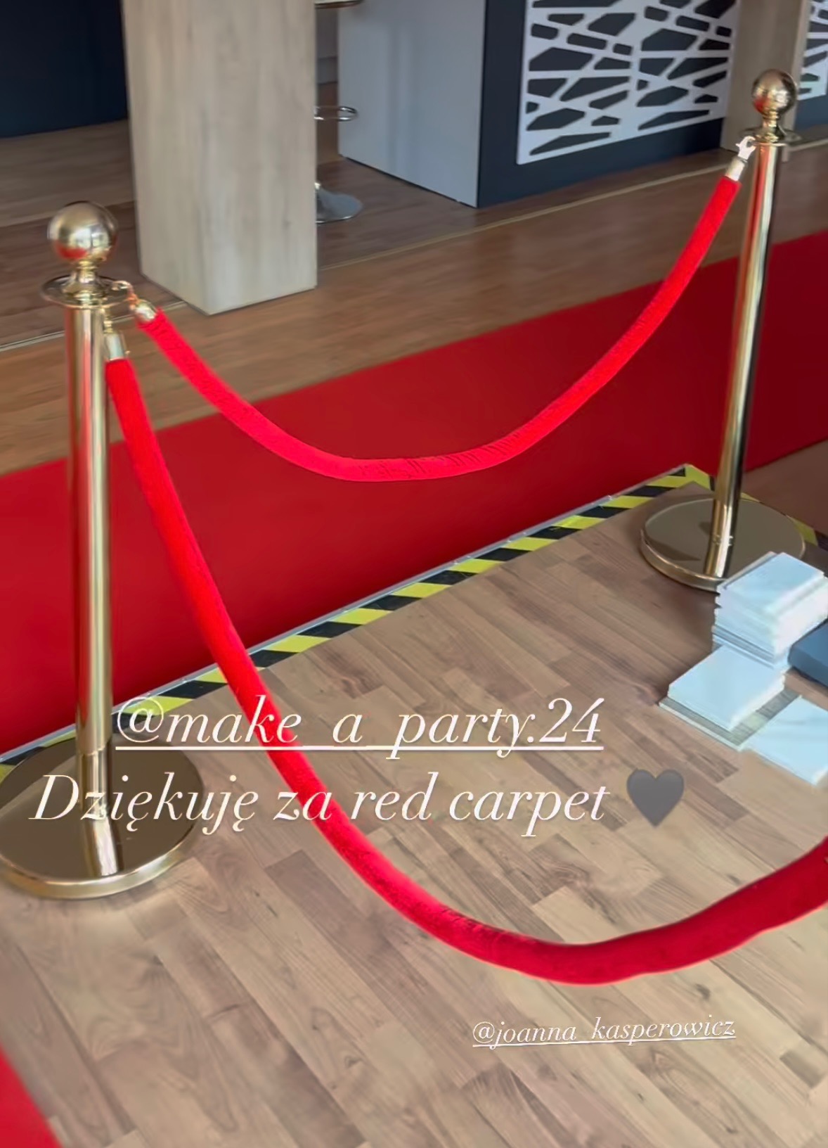 Czerwony dywan i złote słupki z linami w Tuchorzy. Dekoracja eventowa, elegancja i prestiż. Detal z podłogą imitującą drewno i fragmentem czerwonego dywanu.