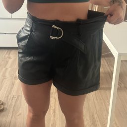 Twój Ulubiony Trener Łukasz Waś - Kobieta w sportowym topie i skórzanych szortach, trzymająca luźny pas, demonstrująca utratę wagi, widoczny tatuaż na ramieniu.