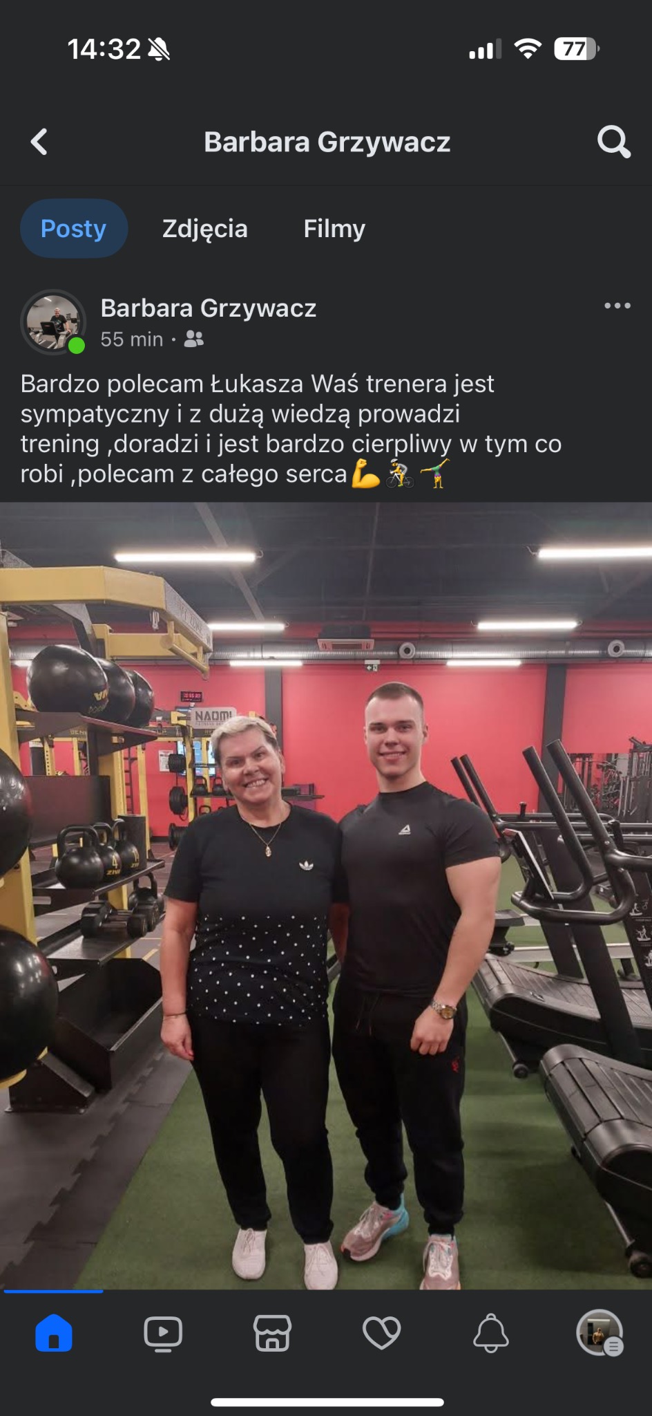 Kobieta i mężczyzna, prawdopodobnie trener personalny i jego klientka, stoją uśmiechnięci w siłowni na tle sprzętu do ćwiczeń, w tym kettlebells i bieżnie.