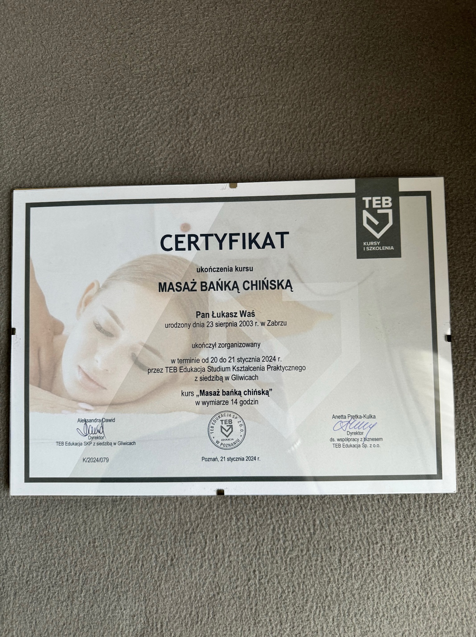 Certyfikat ukończenia kursu masażu bańką chińską, wydany przez TEB Edukacja, z pieczęciami i podpisami dyrektorów, leżący na szarym tle.