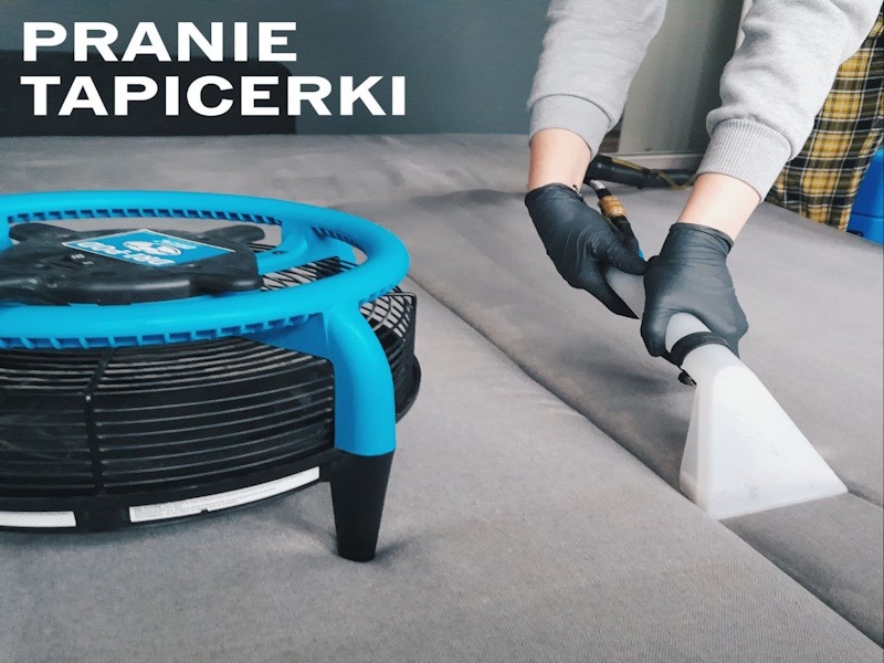 Szary narożnik czyszczony na mokro, widoczny niebieski wentylator wspomagający suszenie, ręce w czarnych rękawicach obsługują dyszę odkurzacza piorącego.