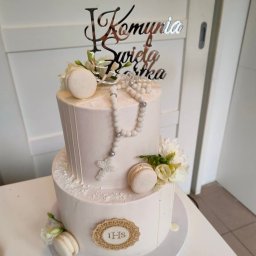Wit - Al IWONA WITALSKA - Dwupiętrowy tort w jasnych barwach, udekorowany makaronikami, białymi kwiatami, różańcem i srebrnym napisem 'I Komunia Święta Bartka', na białym stole.