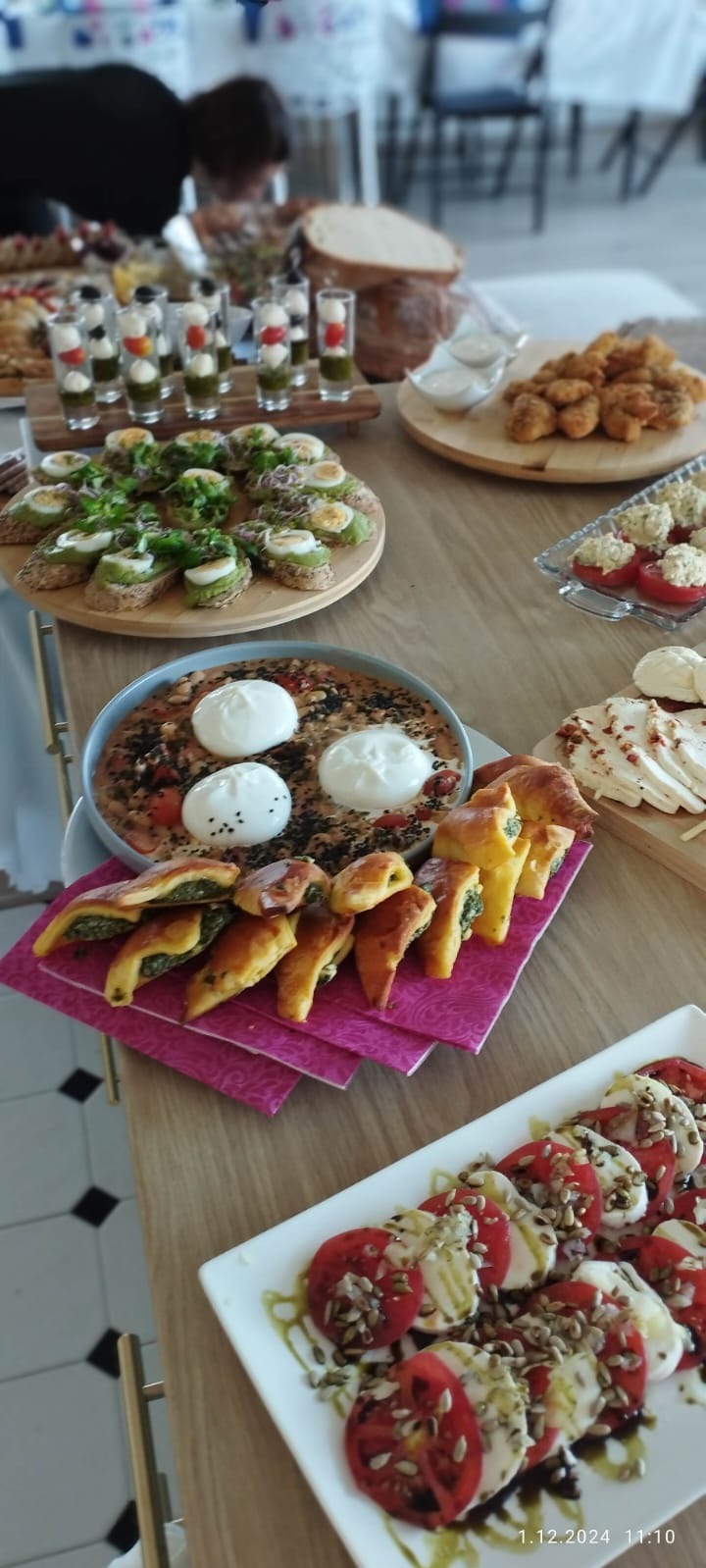 Stół z różnorodnymi przekąskami: koreczki z jajkiem i awokado, mini-szaszłyki z mozzarelli i pomidorów w kieliszkach, pizza z trzema burratami, zapiekane pierożki ze szpinakiem, sałatka caprese...