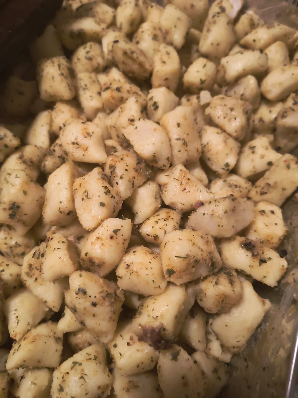 Kopytka ziemniaczane doprawione ziołami w metalowej misce, widok z góry, oświetlenie kuchenne.