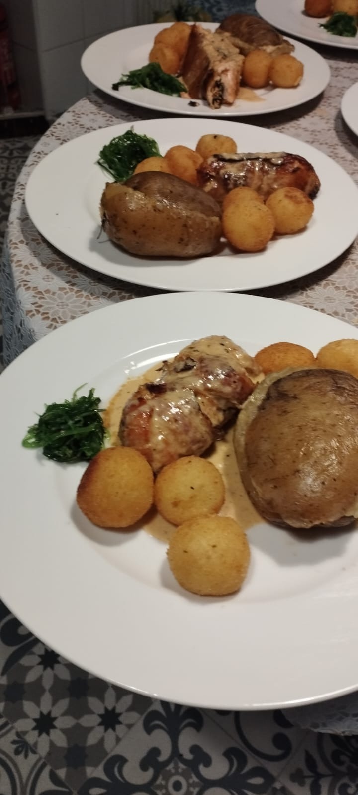 Dwa talerze z pieczonym ziemniakiem, mięsem w sosie i smażonymi kulkami ziemniaczanymi, udekorowane zielonymi warzywami; jeden talerz w ostrym fokusie, drugi w tle.