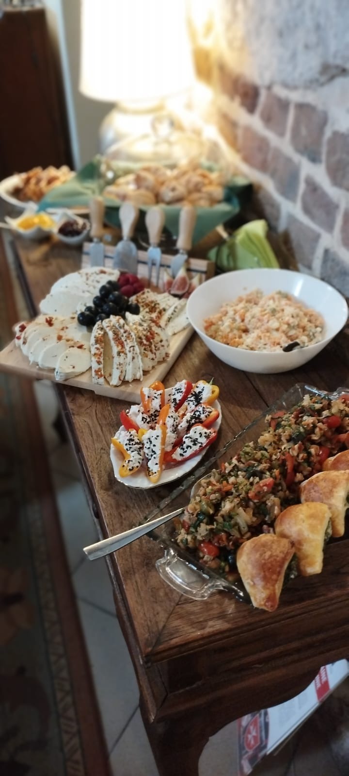 Stół z różnorodnymi przekąskami: deska serów z winogronami i figami, papryka faszerowana białym serem posypana czarnuszką, sałatka jarzynowa w białej misce, paszteciki ze szpinakiem i warzywa...