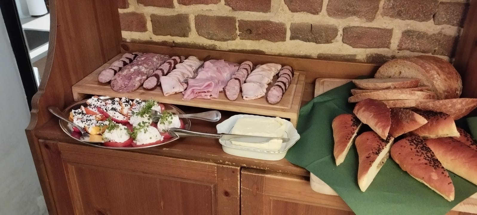 Stół szwedzki w Lusinie z różnymi rodzajami wędlin, pieczywa, masła i sałatki z pomidorów i sera.