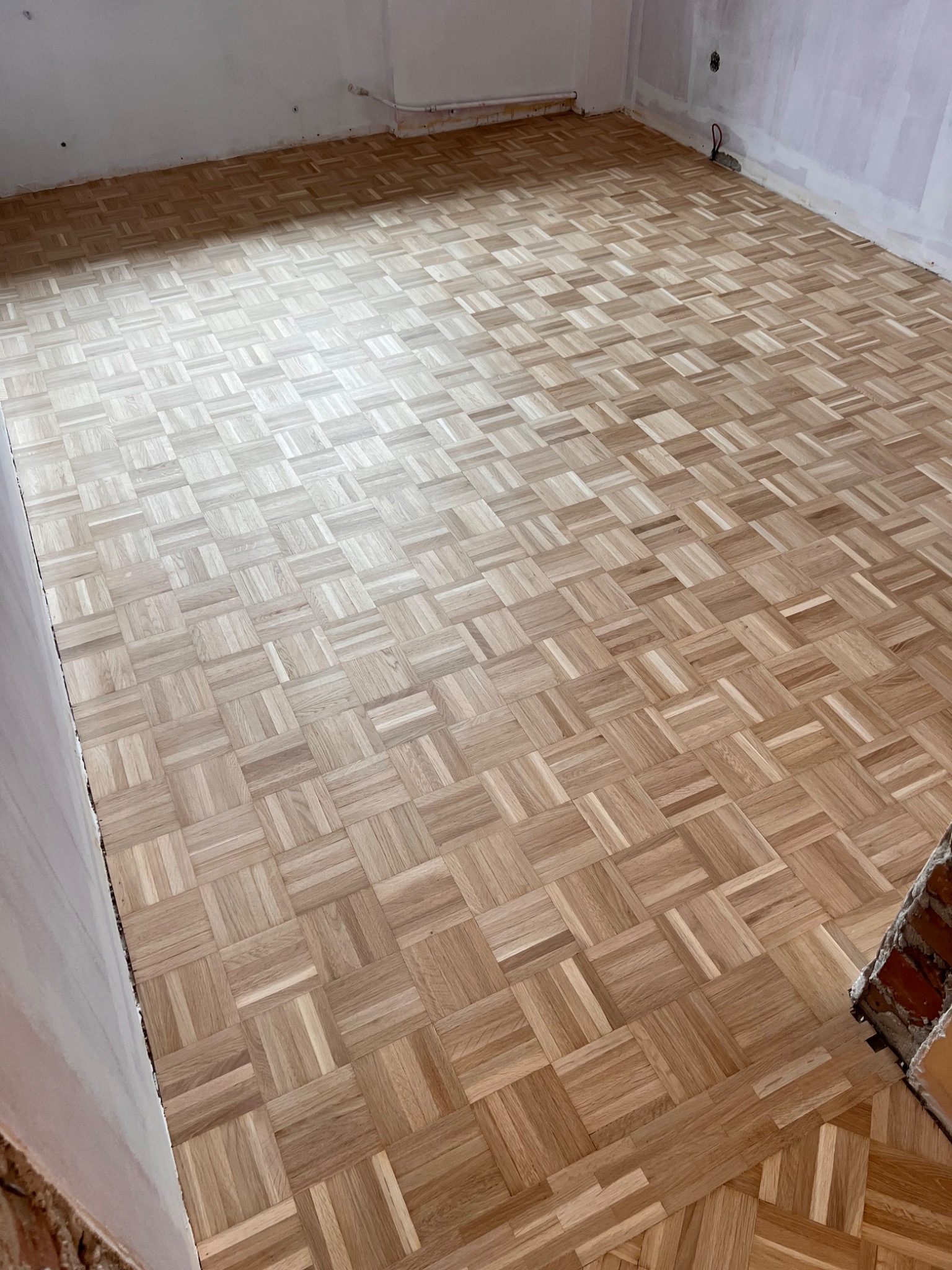 Ułożona parkietowa podłoga w jodełkę z jasnego drewna w trakcie renowacji, widoczne surowe ściany przygotowane do malowania.