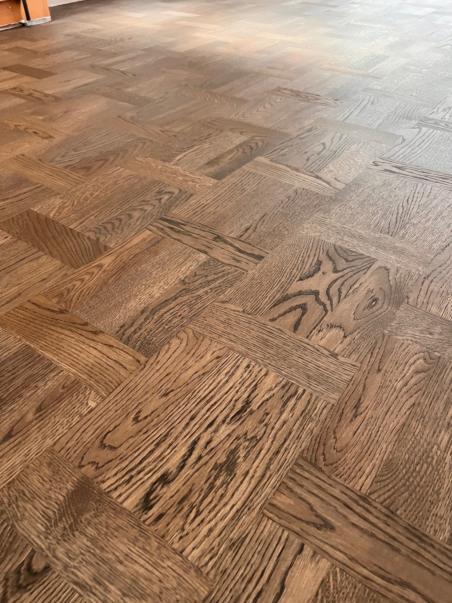 Parkiet ułożony w jodełkę francuską, z wyraźnym usłojeniem drewna i ciepłym odcieniem brązu, wypełniający całą klatkę zdjęcia.