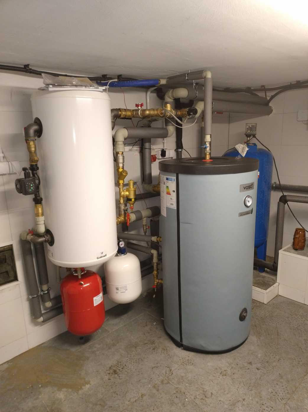 Kotłownia z dwoma zbiornikami: białym Galmet i szarym Vast, połączone rurami z zaworami, widoczny również niebieski hydrofor.
