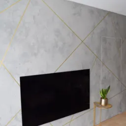 Ściana z szarego mikrocementu z geometrycznym wzorem ze złotych linii, wkomponowany telewizor, złoty stolik z rośliną w złotym wazonie.