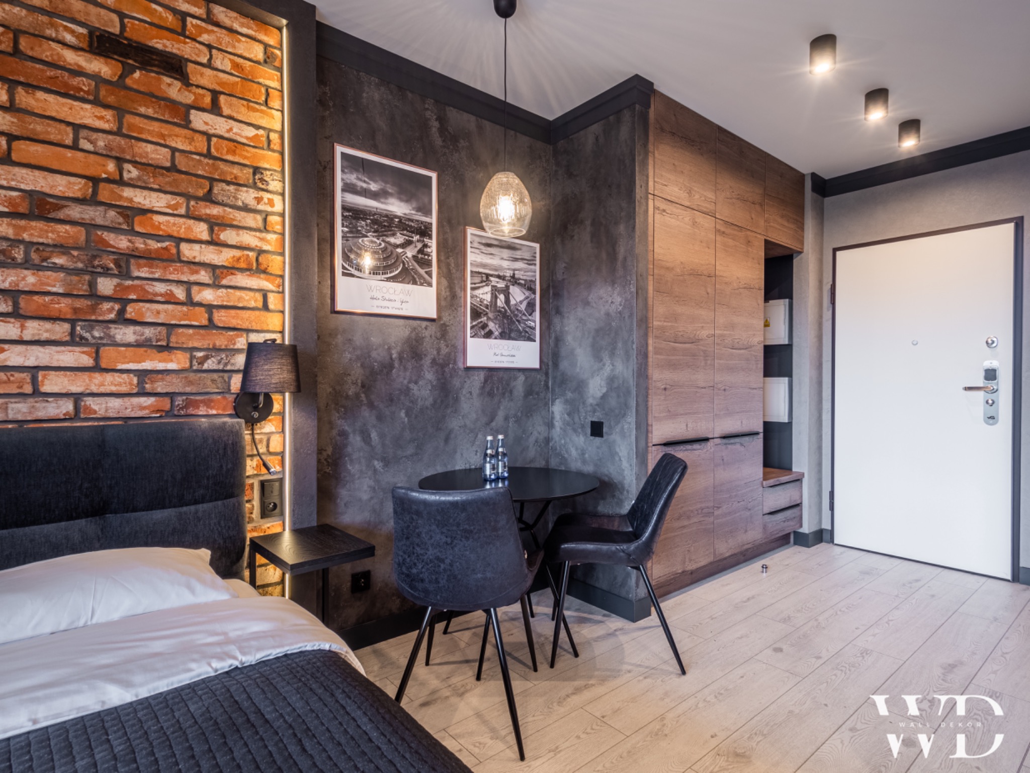 Nowoczesne wnętrze mieszkania z ceglaną ścianą, betonową strukturą, drewnianą zabudową, okrągłym stolikiem i designerskim oświetleniem.