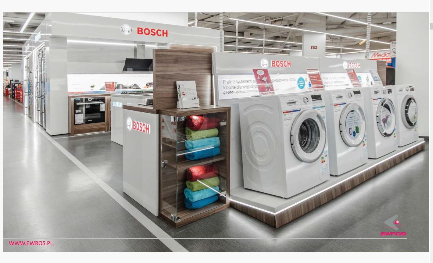 Ekspozycja sprzętu AGD marki Bosch w salonie: pralki automatyczne i zabudowa meblowa z piekarnikiem oraz szafka ekspozycyjna z kolorowymi ręcznikami.