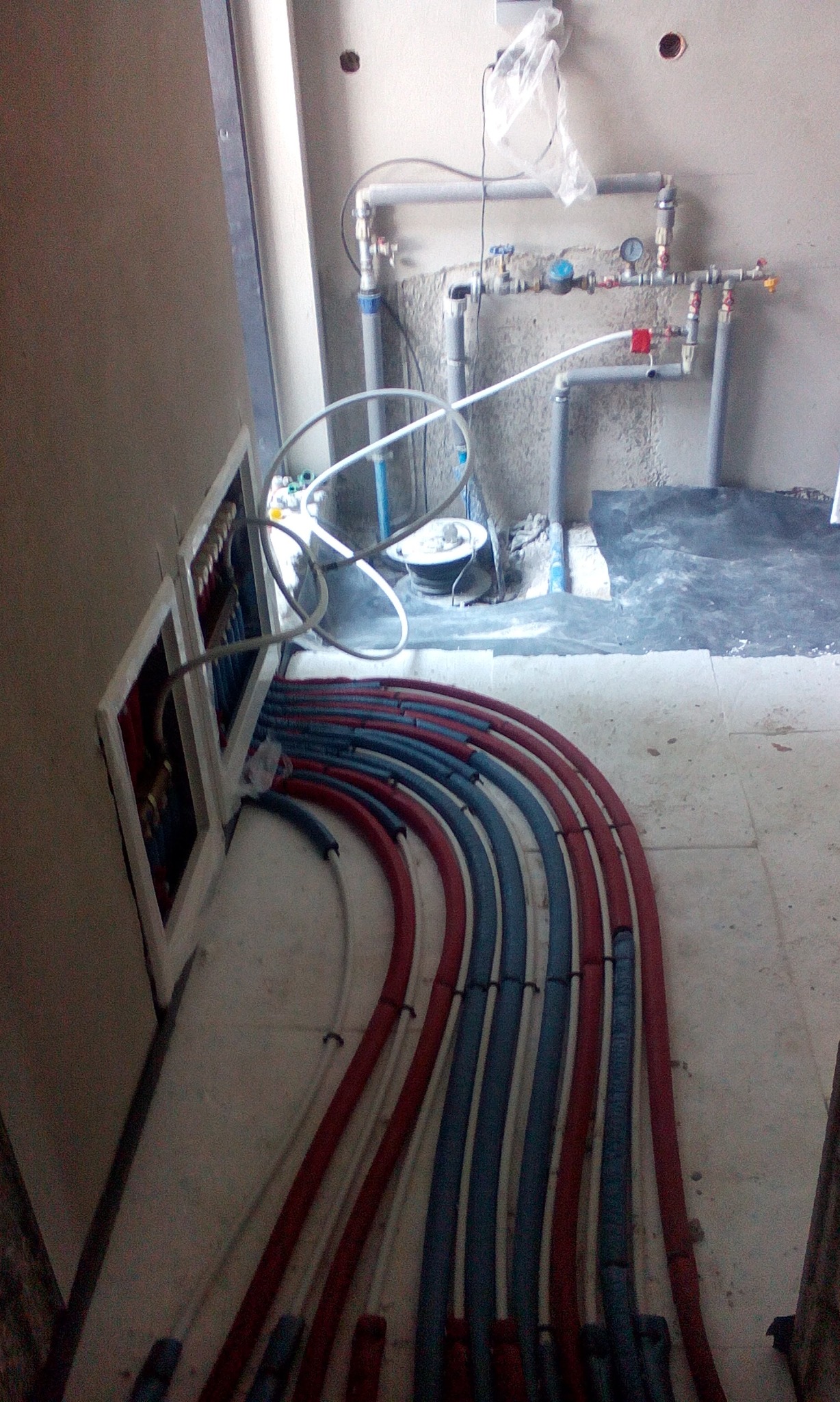 Rozdzielacz instalacji grzewczej i wodnej z rurami PEX w kolorach czerwonym i niebieskim podczas montażu w surowym stanie.