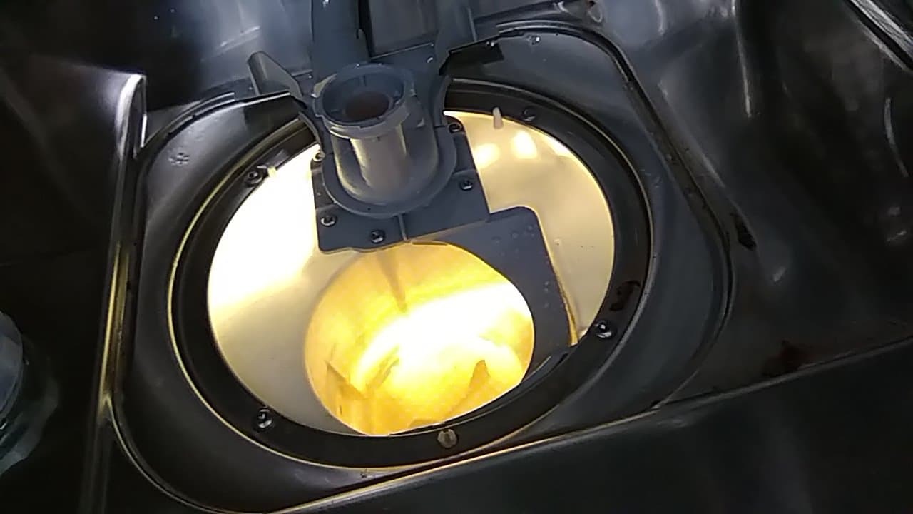 Wnętrze zmywarki z widocznym elementem grzewczym i dyszą natryskową, oświetlone ciepłym światłem, ukazujące szczegóły konstrukcyjne i stan techniczny urządzenia.