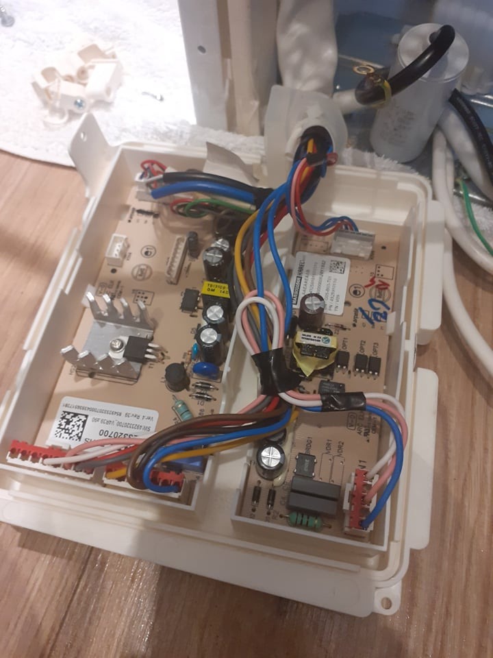 Otwarta obudowa modułu sterującego urządzenia AGD z widoczną płytką drukowaną, przewodami w różnych kolorach i elementami elektronicznymi. Widoczne ślady naprawy w postaci taśmy izolacyjnej.