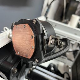 AERO SERWIS Damian Chromiak - Miedziana podstawa chłodzenia wodnego procesora, przymocowana śrubami do czarnej obudowy, z widocznymi przewodami i elementami mocującymi wewnątrz obudowy komputera.