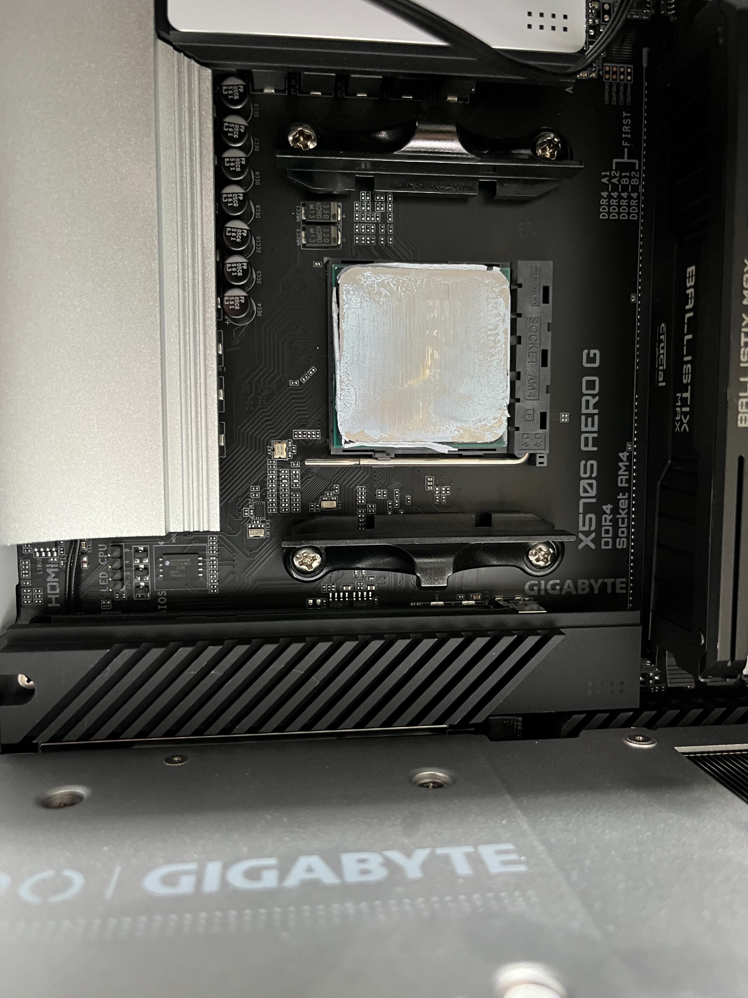 Płyta główna Gigabyte X570S AERO G z socketem AM4, pokryta grubą warstwą białej pasty termoprzewodzącej na procesorze AMD, widoczne moduły pamięci Crucial Ballistix Max DDR4.