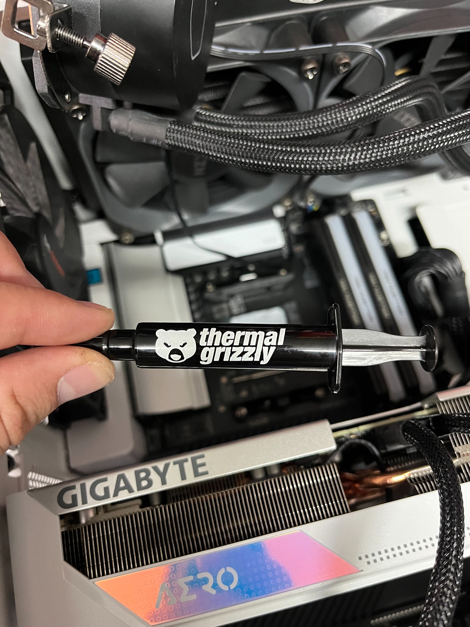 Nakładanie pasty termoprzewodzącej Thermal Grizzly na procesor AMD Ryzen 9 5900x wewnątrz stacji roboczej, widoczna karta graficzna Gigabyte AERO i chłodzenie wodne.