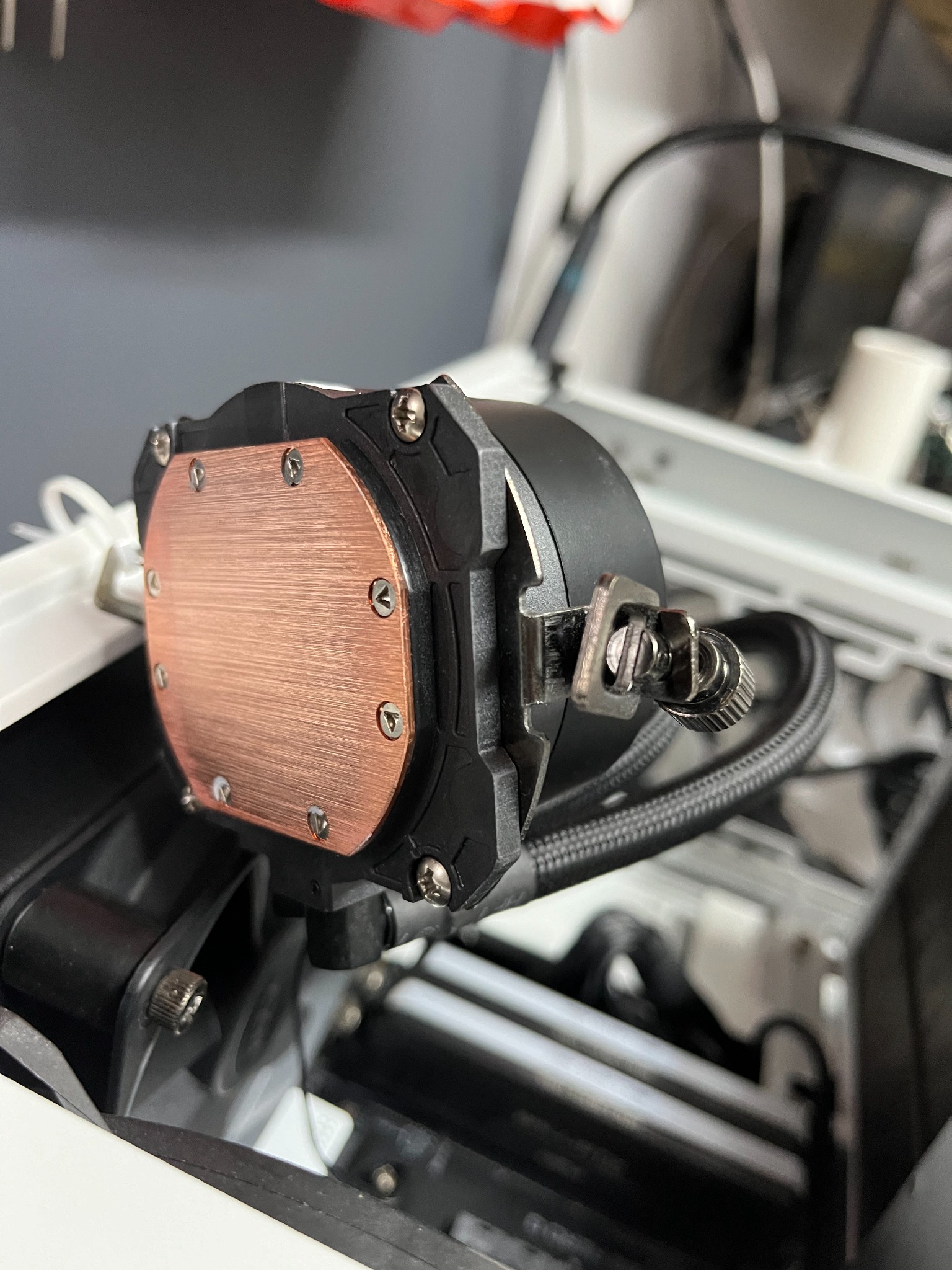 Miedziana podstawa chłodzenia wodnego procesora, przymocowana śrubami do czarnej obudowy, z widocznymi przewodami i elementami mocującymi wewnątrz obudowy komputera.