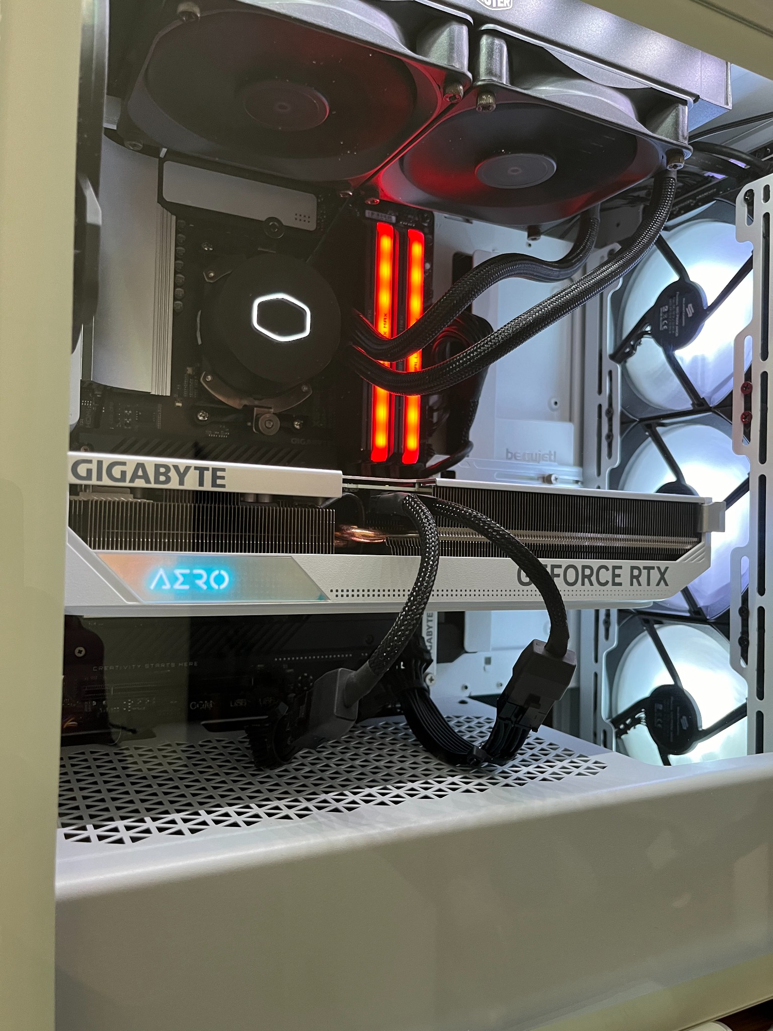 Wnętrze białej obudowy komputera stacjonarnego z zamontowaną kartą graficzną Gigabyte AERO GeForce RTX, chłodzeniem procesora Cooler Master z podświetlanym logo oraz wentylatorami z podświetleniem...
