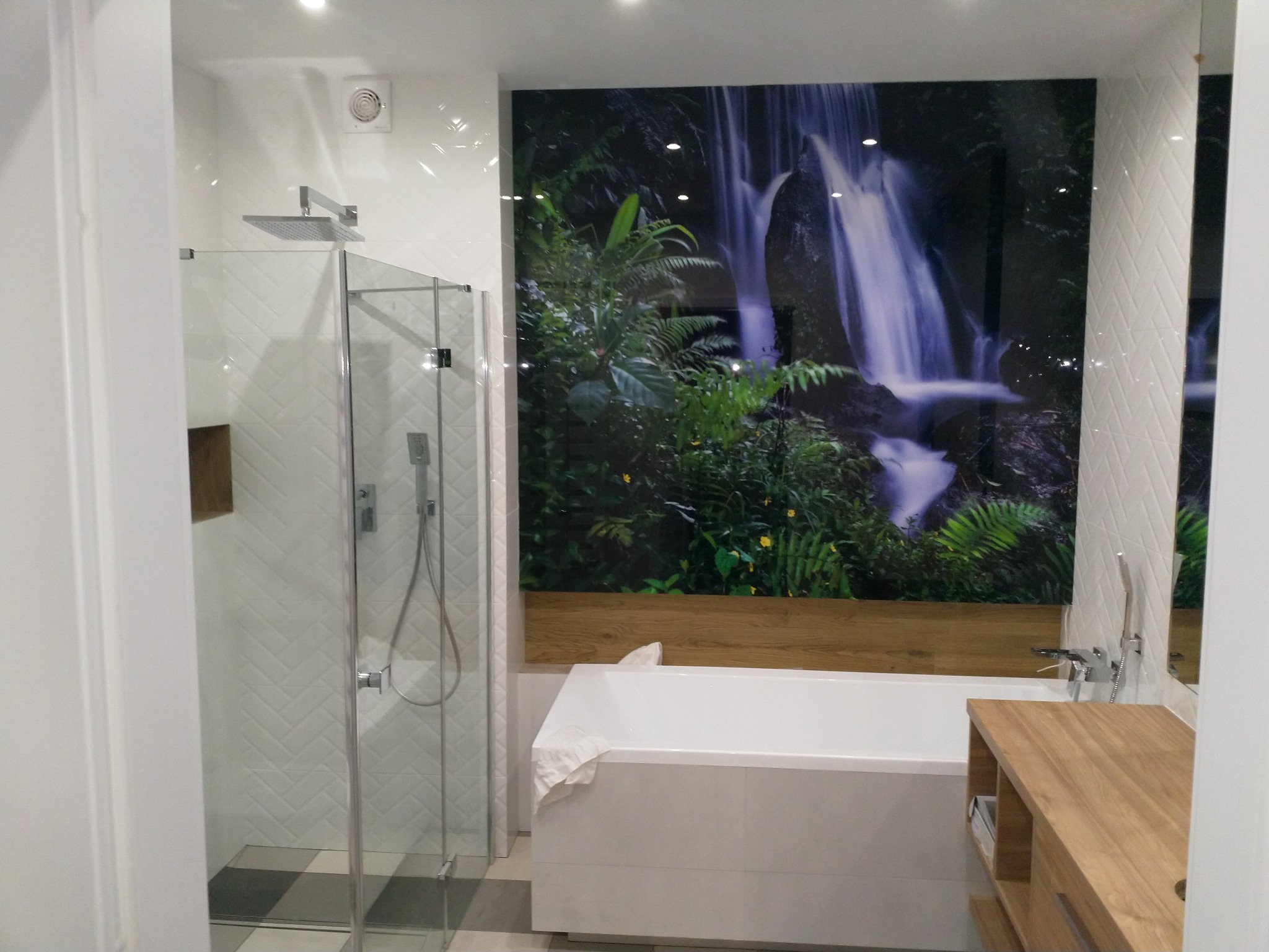 Nowoczesna łazienka z kabiną prysznicową, białą wanną i fototapetą z motywem wodospadu w dżungli, podkreślającą naturalny charakter wnętrza.