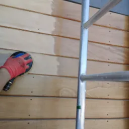 Szlifowanie drewnianej boazerii za pomocą szlifierki oscylacyjnej, widoczny fragment rusztowania i ślady po szpachlowaniu między deskami.