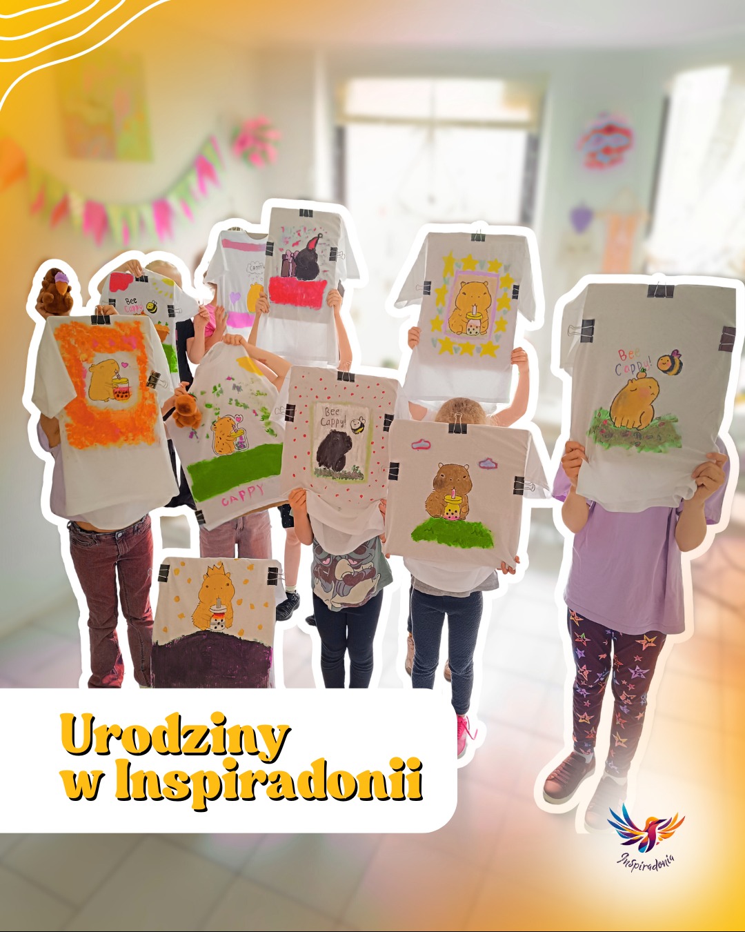 Dzieci prezentują własnoręcznie pomalowane koszulki z motywem kapibary na urodzinach w Inspiradonii, wiszące na wieszakach, z dekoracjami w tle.