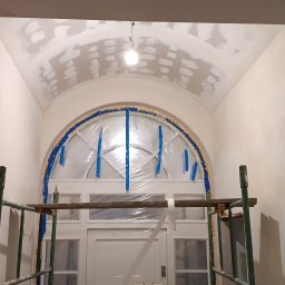 Paweł Radzymiński - Korytarz w trakcie prac wykończeniowych: ściany pokryte gładzią, sufit łukowy z widocznymi łatami, oklejone folią drzwi łukowe, rusztowanie w dolnej części kadru.