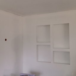 Paweł Radzymiński - Świeżo pomalowane na biało wnętrze z wnęką na ścianie, widoczne puszki elektryczne i rolka tapety na podłodze.