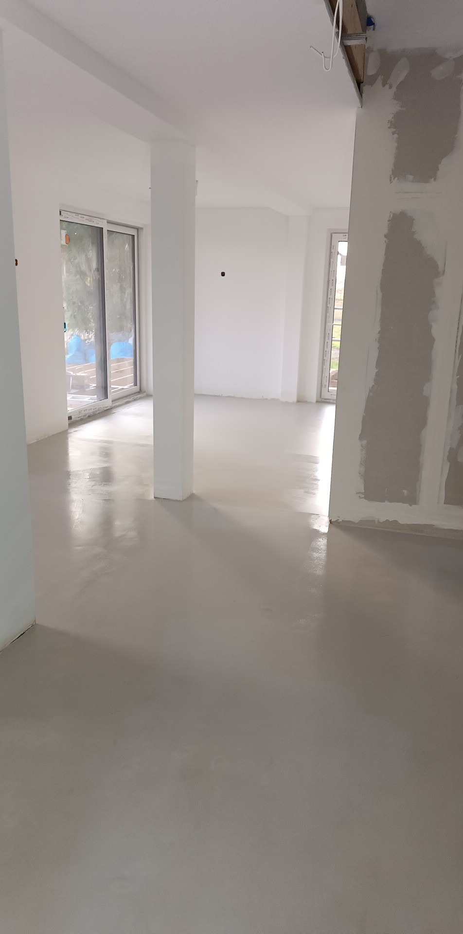 Wnętrze w trakcie prac wykończeniowych: świeżo wylana, jasnoszara posadzka samopoziomująca, ściany przygotowane pod malowanie, widoczne profile sufitowe.