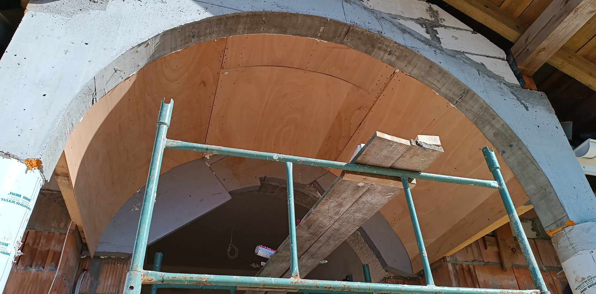 Łuk z płyty OSB w trakcie budowy, widoczne szalunki i rusztowanie, surowy beton i cegła.