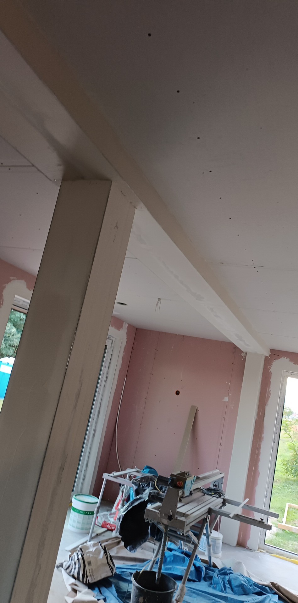 Wnętrze w trakcie prac wykończeniowych: ściany obłożone płytami karton-gips, widoczna konstrukcja sufitu podwieszanego, narzędzia i materiały budowlane na podłodze.