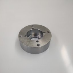 QBIG IRENEUSZ SŁODKOWSKI I WSPÓLNICY SPÓŁKA KOMANDYTOWA - Metalowy pierścień z otworami, obrobiony na tokarce, leżący na białym tle. Widoczne ślady obróbki skrawaniem.